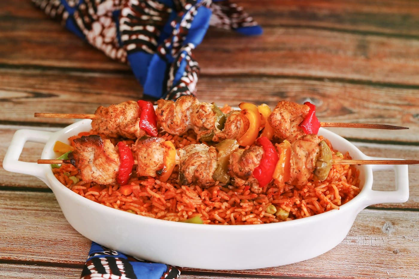 Jollof rice with grilled chicken skewers in a white dish