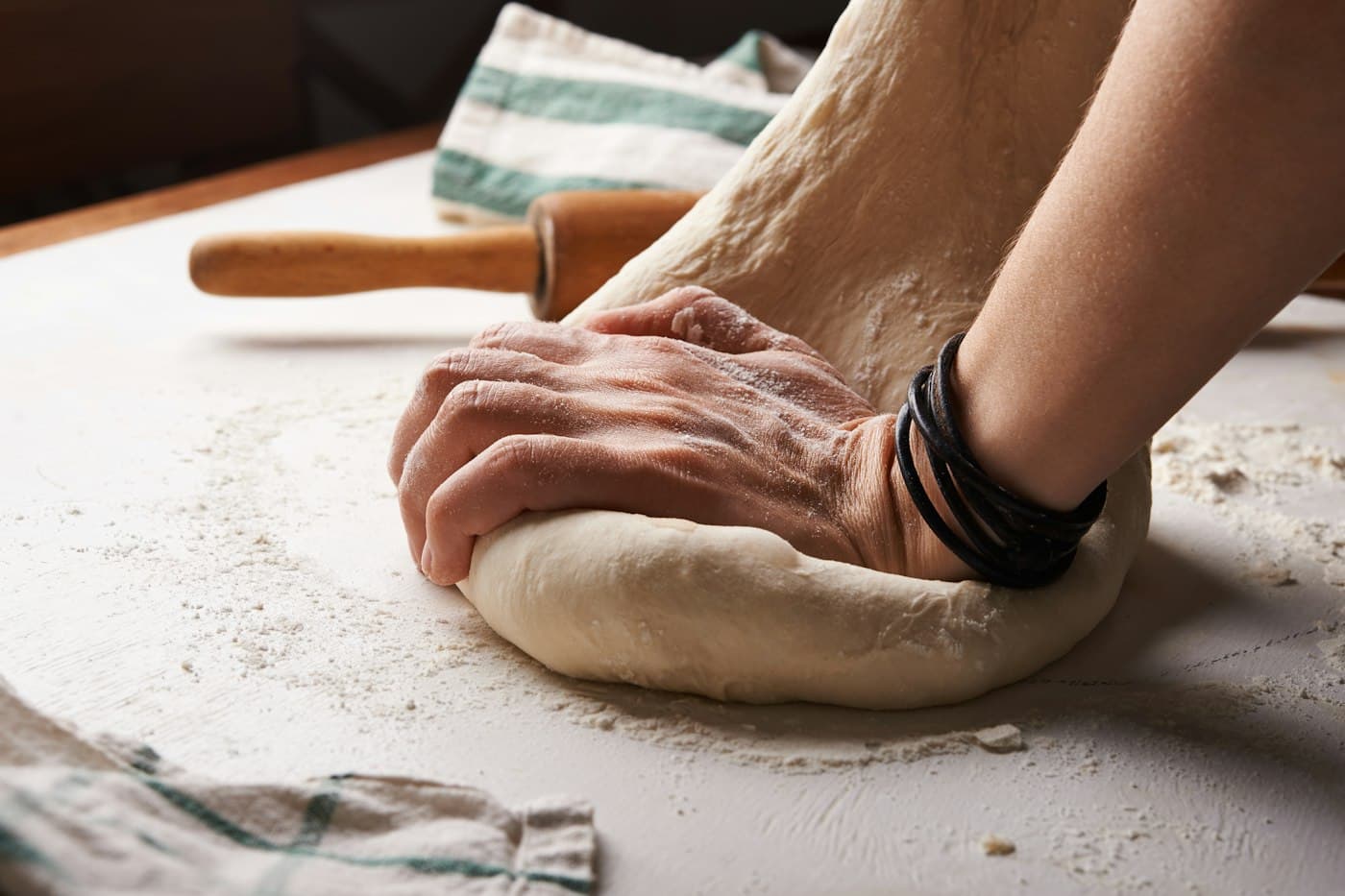 Hands kneading dough beside a wooden rolling pin